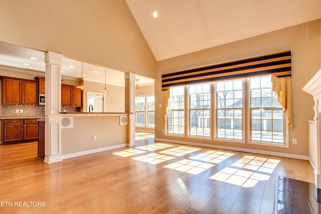 unfurnished living room with high vaulted ceiling, plenty of natural light, light wood-type flooring, and ornate columns