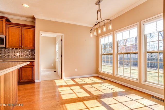 kitchen featuring tasteful backsplash, ornamental molding, decorative light fixtures, and light wood-type flooring