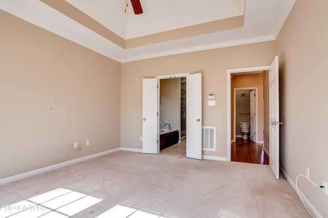 unfurnished bedroom featuring crown molding, carpet flooring, ensuite bathroom, and a tray ceiling