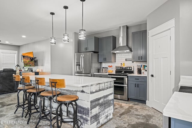 kitchen with gray cabinetry, decorative light fixtures, appliances with stainless steel finishes, a kitchen breakfast bar, and wall chimney range hood