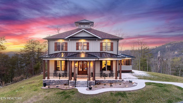 view of front of property with driveway, covered porch, a front lawn, and a standing seam roof