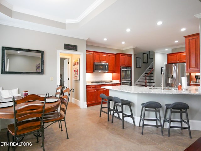 kitchen featuring appliances with stainless steel finishes, a breakfast bar, backsplash, ornamental molding, and light stone countertops