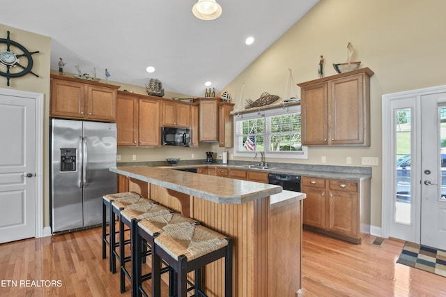 kitchen featuring a kitchen island, sink, a kitchen breakfast bar, light hardwood / wood-style floors, and black appliances