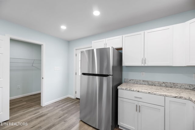 kitchen featuring light hardwood / wood-style flooring, stainless steel fridge, light stone countertops, and white cabinets