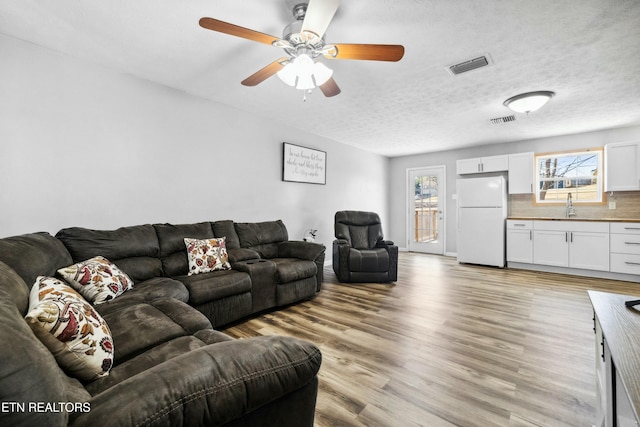 living room with ceiling fan, sink, light hardwood / wood-style floors, and a textured ceiling