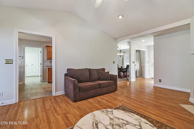 living room with vaulted ceiling, ceiling fan with notable chandelier, and light hardwood / wood-style flooring