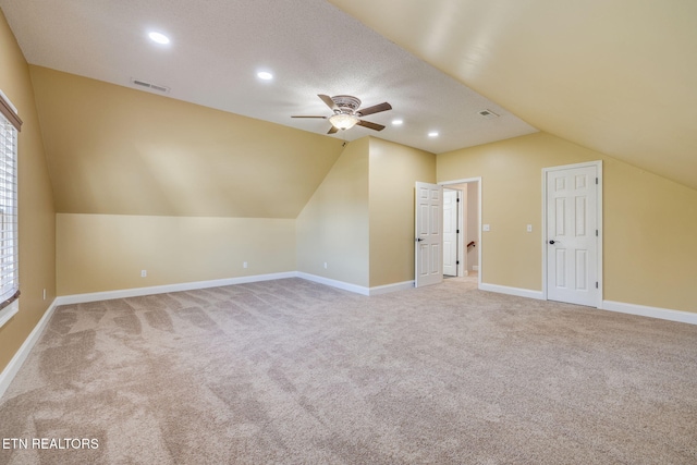 additional living space with light carpet, vaulted ceiling, ceiling fan, and a textured ceiling