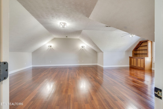 additional living space with vaulted ceiling, built in shelves, dark wood-type flooring, and a textured ceiling