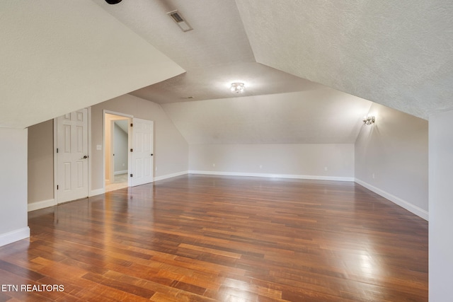 additional living space with lofted ceiling, dark hardwood / wood-style flooring, and a textured ceiling