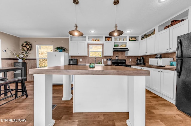 kitchen featuring a kitchen island, butcher block countertops, white cabinetry, hanging light fixtures, and black appliances