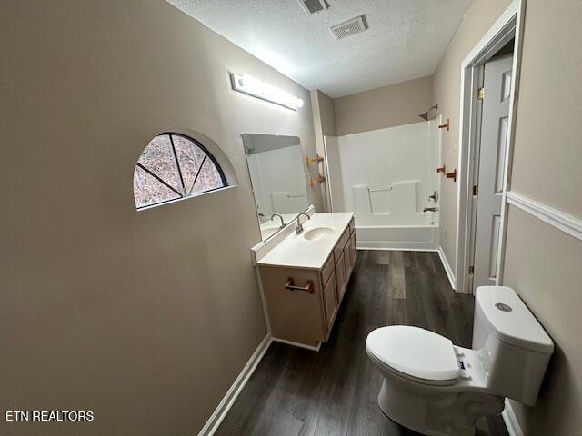 full bathroom with wood-type flooring, vanity, toilet, a textured ceiling, and washtub / shower combination