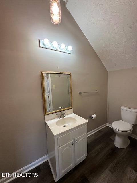 bathroom featuring vaulted ceiling, wood-type flooring, vanity, toilet, and a textured ceiling