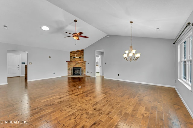 unfurnished living room with hardwood / wood-style flooring, vaulted ceiling, a stone fireplace, and ceiling fan with notable chandelier