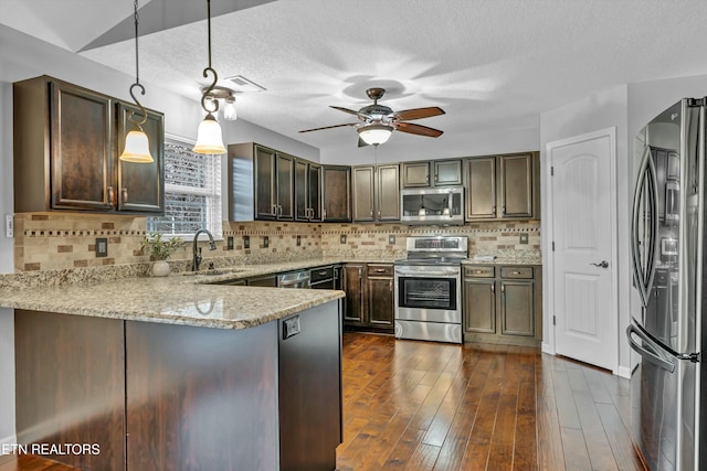 kitchen with decorative light fixtures, sink, light stone counters, kitchen peninsula, and stainless steel appliances