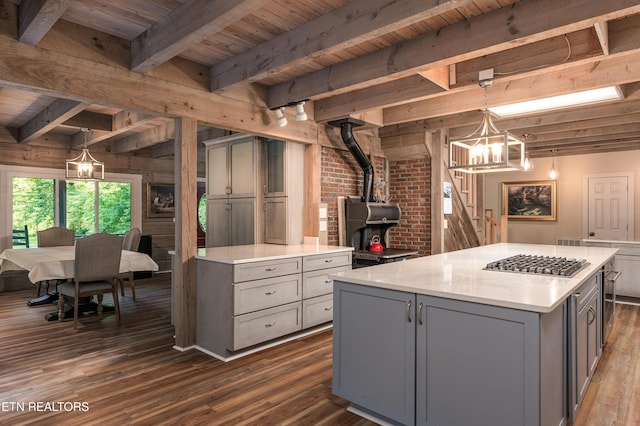 kitchen with gray cabinets, a kitchen island, pendant lighting, stainless steel gas stovetop, and a wood stove