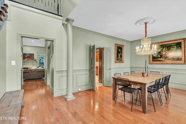 dining room featuring crown molding, decorative columns, light hardwood / wood-style flooring, and a notable chandelier