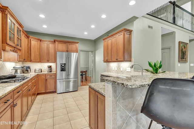 kitchen featuring stainless steel appliances, a kitchen breakfast bar, light stone countertops, and light tile patterned floors