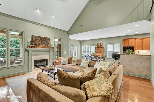 living room featuring ornamental molding, high vaulted ceiling, a tiled fireplace, and light hardwood / wood-style floors