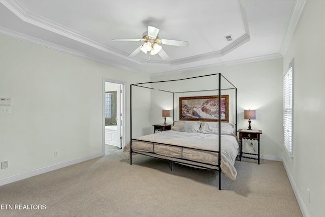 carpeted bedroom with a tray ceiling, ensuite bath, ornamental molding, and ceiling fan