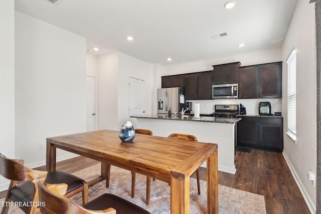 kitchen featuring dark hardwood / wood-style floors, an island with sink, dark stone countertops, stainless steel appliances, and a healthy amount of sunlight