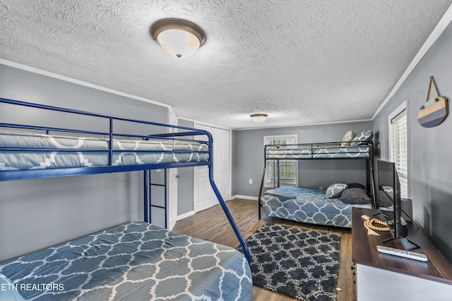 bedroom featuring multiple windows, wood-type flooring, ornamental molding, and a textured ceiling