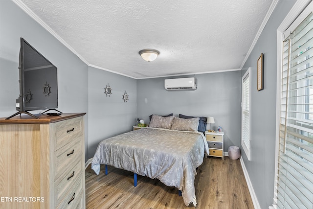 bedroom featuring crown molding, a textured ceiling, a wall mounted AC, and light wood-type flooring