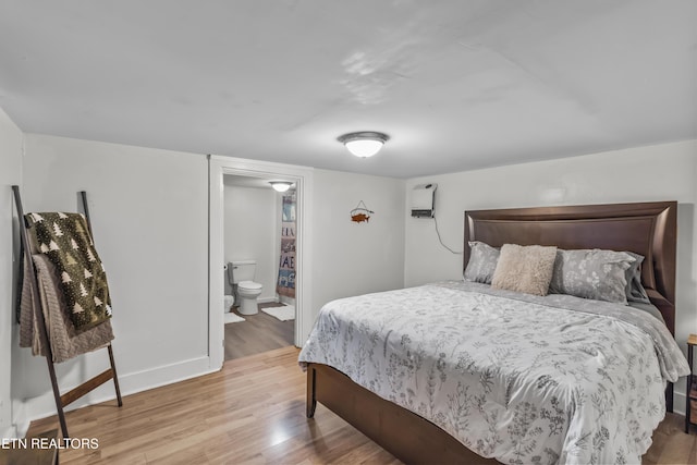 bedroom featuring hardwood / wood-style floors, a wall unit AC, and ensuite bath