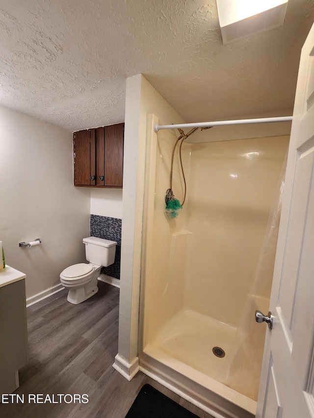 bathroom with hardwood / wood-style flooring, a textured ceiling, toilet, and a shower