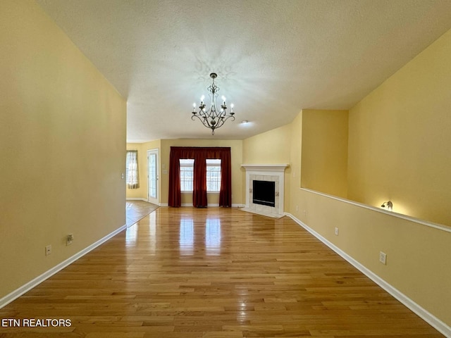 unfurnished living room featuring a tile fireplace, a chandelier, wood-type flooring, and a textured ceiling