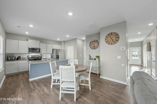 kitchen with appliances with stainless steel finishes, dark hardwood / wood-style floors, a breakfast bar area, light stone countertops, and a center island with sink