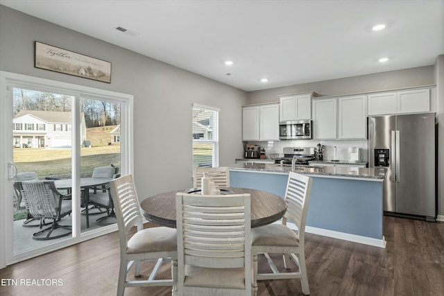 kitchen with a kitchen island with sink, stainless steel appliances, dark hardwood / wood-style floors, light stone counters, and white cabinets