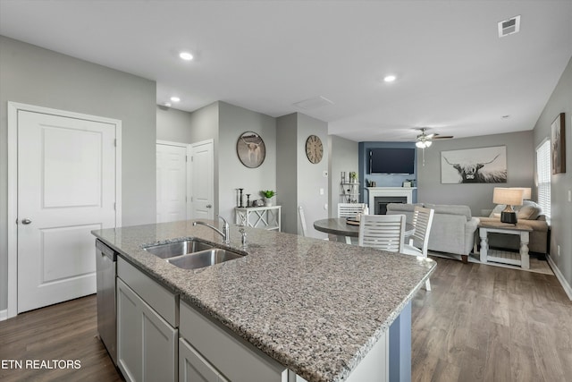 kitchen with dishwasher, sink, hardwood / wood-style flooring, light stone countertops, and a center island with sink