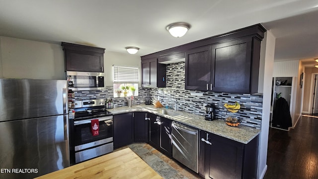 kitchen featuring stainless steel appliances, light stone countertops, hardwood / wood-style flooring, and backsplash