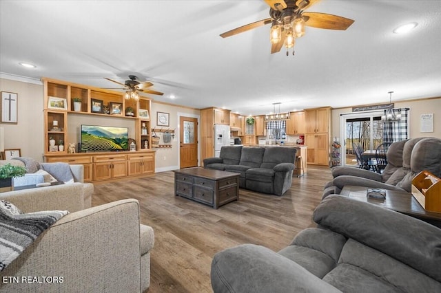 living room featuring ornamental molding, wood-type flooring, and ceiling fan with notable chandelier