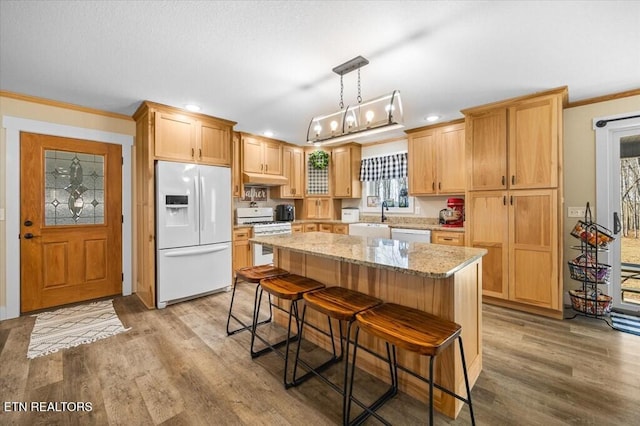 kitchen featuring pendant lighting, white appliances, light stone counters, ornamental molding, and a kitchen island