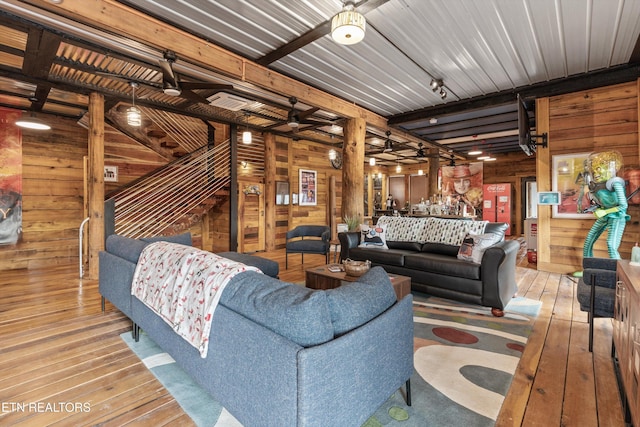 living room with wood walls, stairs, beam ceiling, and wood finished floors