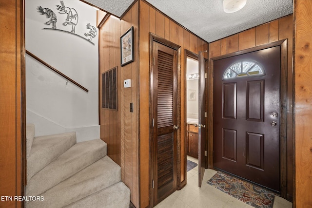 entryway with wooden walls, visible vents, stairway, and a textured ceiling