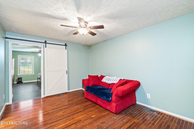 sitting room with dark hardwood / wood-style floors, ceiling fan, a barn door, and a textured ceiling