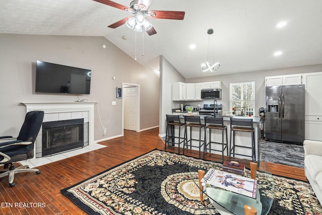 living room with a tile fireplace, lofted ceiling, sink, and dark hardwood / wood-style flooring