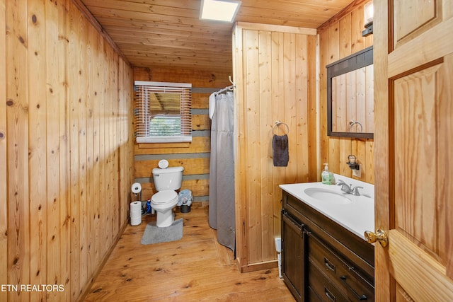 bathroom with toilet, wood walls, wood finished floors, vanity, and wood ceiling