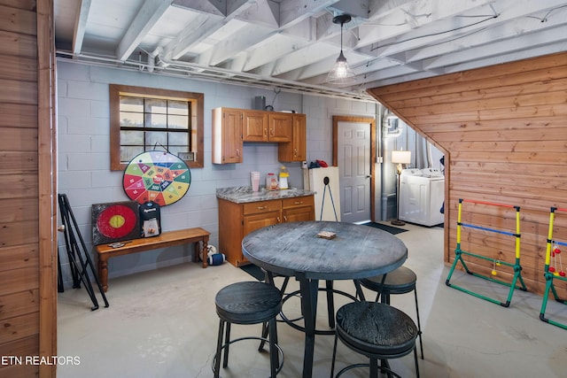 kitchen with concrete block wall, brown cabinets, finished concrete flooring, light stone countertops, and washer / dryer