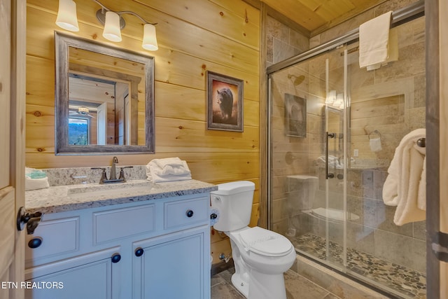 bathroom featuring vanity, wooden walls, a shower with door, and toilet