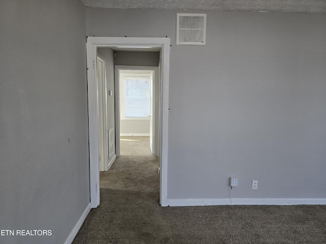 corridor with dark colored carpet and a textured ceiling