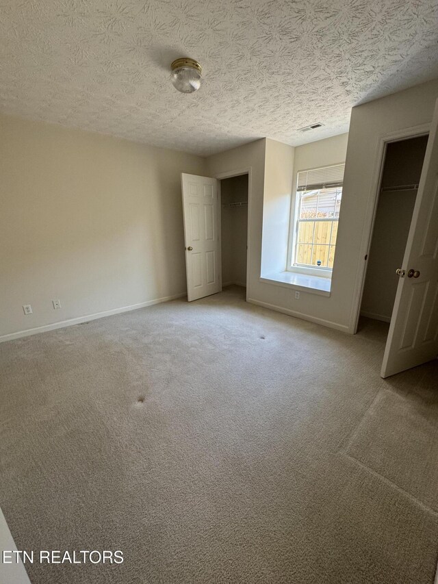 unfurnished bedroom with a walk in closet, a textured ceiling, and carpet flooring