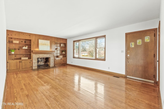 unfurnished living room with built in shelves, a fireplace, and light hardwood / wood-style flooring