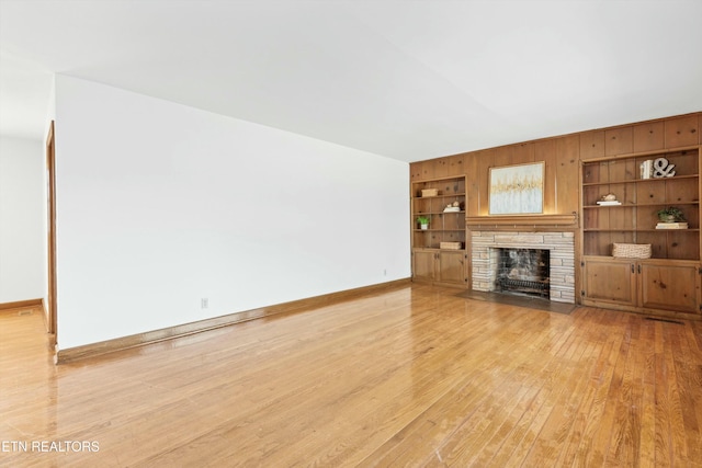 unfurnished living room featuring a stone fireplace, light hardwood / wood-style flooring, and built in features