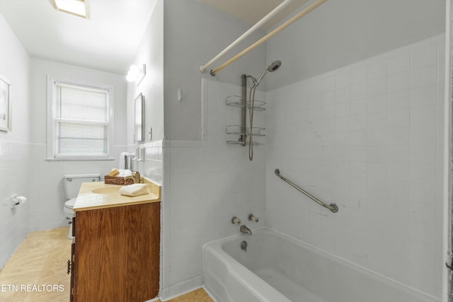 full bathroom with vanity, tiled shower / bath combo, toilet, and tile walls