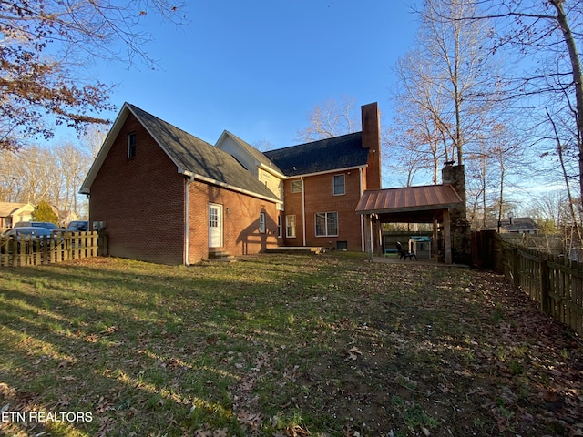 rear view of house featuring entry steps, a lawn, a fenced backyard, a chimney, and brick siding