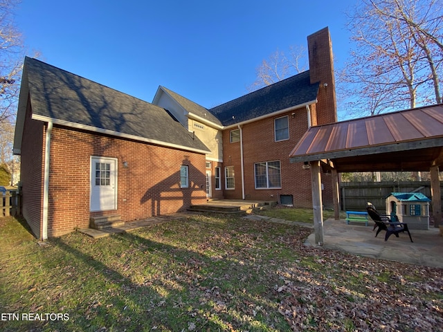 back of house featuring a lawn, a chimney, a gazebo, a patio area, and brick siding