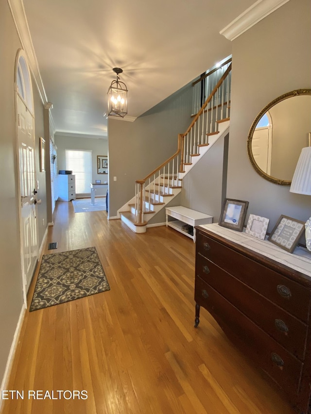 entryway with visible vents, stairway, wood finished floors, crown molding, and a notable chandelier